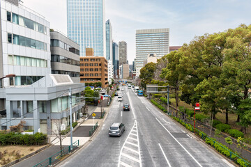Fototapeta na wymiar Urban road lined with office and residential buildings on one side and with a park on the other side in central Tokyo, Japan, on a cloudy spring day