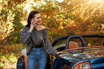 Fototapeta na wymiar Woman in jeans and in a grey sweater speaks by phone near cabriolet