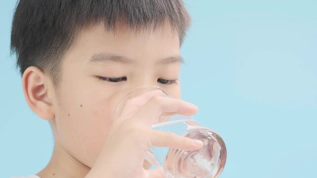 Selective focus young Asian boy drink water from glass on blue background