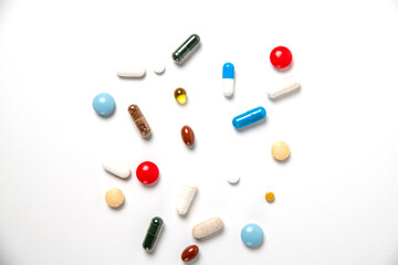 many pills of different shapes and different colors on a white background