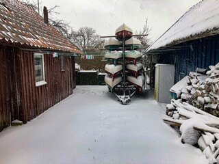 Snowy Yard with Stacked Canoes between Wooden Sheds in Winter Stillness