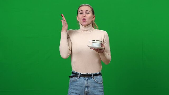 Young woman drinking tea and burning tongue. Slim Caucasian lady burnt with hot drink on green screen. Chromakey background.