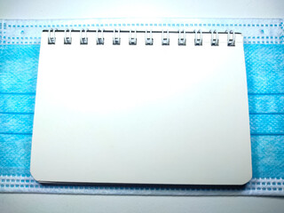 Selective focus of face mask and notebook on white background with copy space.