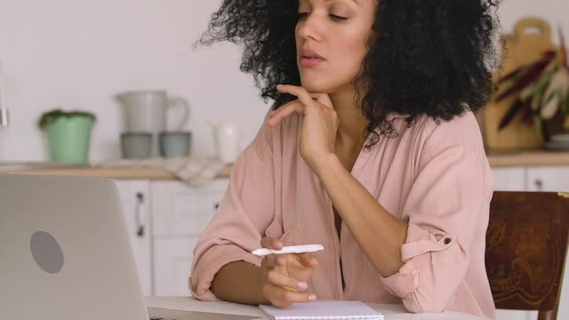 African American woman studying online, remote working using laptop while taking notes in notebook. Black female posing sitting at table in bright kitchen. Close up. Slow motion ready, 4K at 59.97fps.