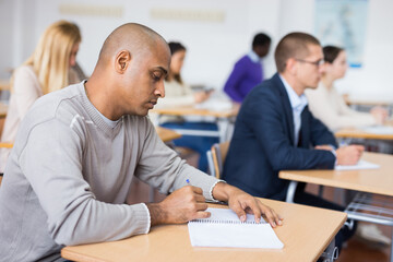 Fototapeta premium Young positive man listening to lecture taking notes at adult education class