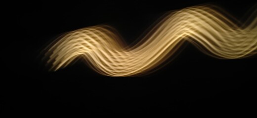 Closeup of Golden yellow Neon light wave pattern abstract flowing through the isolated black background made with long exposure , light painting technique . Copy space . 