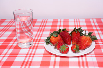 Ripe red strawberries on a white plate with a glass of water.