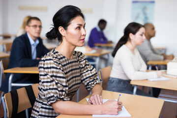 Concentrated asian woman listening to lecture in classroom with group of adult people. Postgraduate...