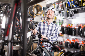 Fototapeta na wymiar interested man in helmet chooses for himself sports bike in bicycle shop from a range