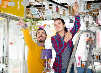 Glad man in shop of home appliances points to stylish and fashionable model lamp