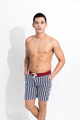 Fototapeta na wymiar Young muscular guy in striped beach shorts sunbathing at studio shot isolated on white background. Fashion summer concept.