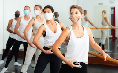 Fototapeta na wymiar Multiethnic dancers in medical masks training near barre during COVID-19 pandemic.