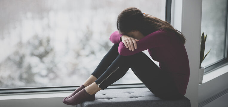Sad crying young woman hiding face in sadness alone at home in isolation. Mental health problem social anxiety panic attack ptsd effects from the coronavirus pandemic.