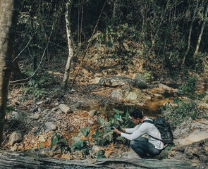 Young man photographer shooting near stream in forest