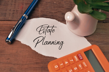Top view of pen, calculator, plant and torn paper written with ESTATE PLANNING