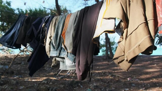 Clothes are dried on a clothesline in a poor African village. Various Colourful clothes, T-shirts, pants hanging out to dry on a rope between the palm trees. Lot of Washings are drying outside. Africa