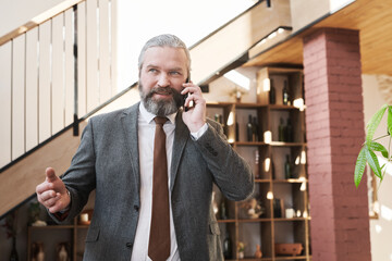 Confident mature businessman having a conversation on mobile phone while going to the meeting in the restaurant