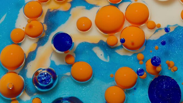 Top view movement of bright oil bubbles in slow motion. Multicolored surface background. Fantastic universe structure of colorful moving orange bubbles. Artistic image of ink drops floating on water