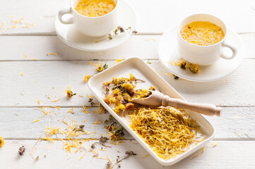 two cups of aromatic flower tea, soothing, medicinal on a white wooden background with dry yellow flowers