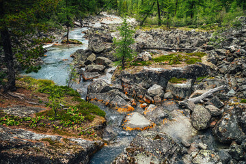 Fototapeta na wymiar Scenic nature background of turquoise clear water stream among rocks with mosses, lichens and wild flora. Atmospheric mountain landscape with transparent mountain creek. Beautiful mountain stream.