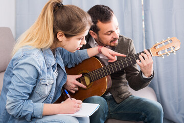 Young american guitar tutor explaining basics to his female client at home