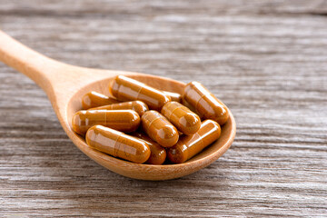 Turmeric powder herbal capsules in wooden spoon isolated on old rustic wooden table background.