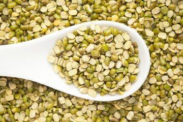 macro Close-up of Organic green Gram (Vigna radiata) or spilt green moong dal unpolished on a white ceramic soup spoon. Top view