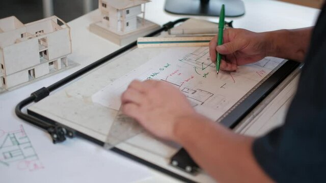An Asian (Thai) architect is working on a white drawing desk. By scribbling on a white construction plan with a pen.