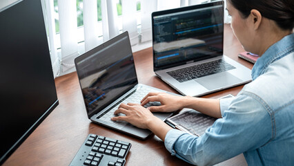 Asian programmer woman looking on multiple computer screen to typing coding database and...
