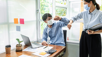 Two business colleagues greet each other by bumping elbows when meeting in office while wearing face mask