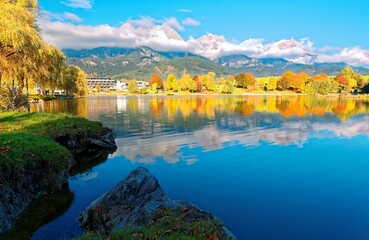 Scenery of beautiful Lake Ritzensee on a sunny autumn day in Saalfelden, Salzburger Land, Austria, with reflections of colorful fall foliage on the peaceful lake & majestic Austrian Alps in background