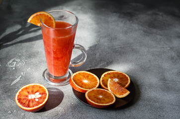 Fresh blood orange juice in a transparent glass on black rough surface with several slices on a...