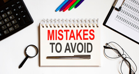 Notepad with the text MISTAKES TO AVOID on a light background, near glasses and office tools