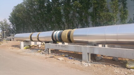 The new black metal pipe with insulated designed to carry pressurized steam is overground parallel to the road.