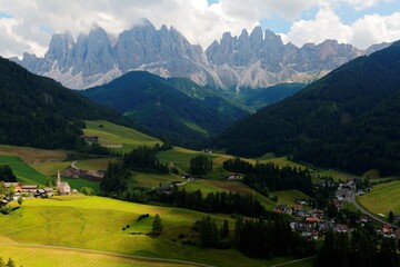 Fototapeta na wymiar Idyllic scenery of Val di Funes on a cloudy summer day with rugged peaks of Odle mountain in background & a church in Village Santa Maddalena in the green grassy valley in Dolomiti, South Tyrol, Italy