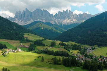 Fototapeta na wymiar Summer scenery of idyllic Val di Funes with rugged peaks of Odle (Geisler) mountain range in background & a church in Village Santa Maddalena in the green grassy valley in Dolomiti, South Tyrol, Italy