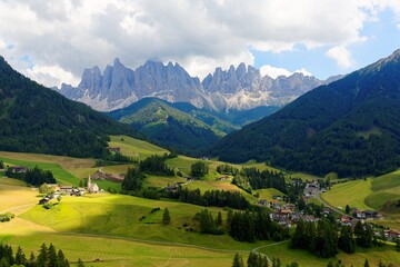 Fototapeta na wymiar Summer scenery of idyllic Val di Funes with rugged peaks of Odle (Geisler) mountain range in background & a church in Village Santa Maddalena in the green grassy valley in Dolomiti, South Tyrol, Italy