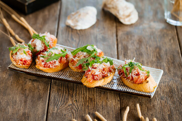 Salmon bruschettas with grated cheese and arugula on the wooden background