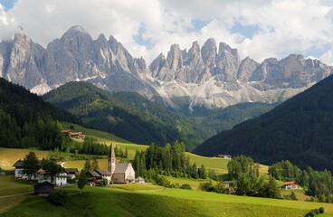 Idyllic scenery of Val di Funes in summer season with rugged peaks of Odle mountain range in background & a church in Village Santa Maddalena in the green grassy valley in Dolomiti, South Tyrol, Italy