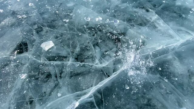 Slow motion video of a piece of ice falling from a height and breaking on the smooth transparent blue ice of frozen Lake Baikal. The ice floe breaks into many fragments. Beautiful ice with deep cracks