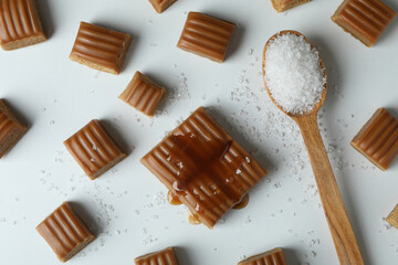 Caramel pieces and spoon of salt on white background