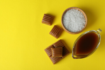 Caramel pieces, sauce and bowl of salt on yellow background