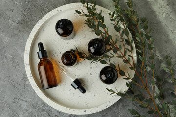 Tray with bottles of eucalyptus oil and branch on gray table