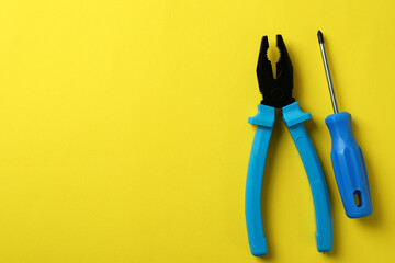 Pliers and screwdriver on yellow background, space for text