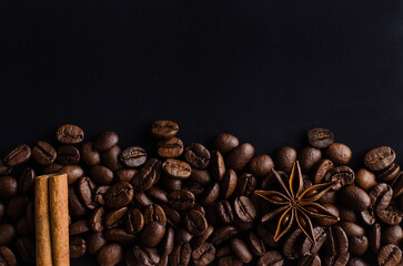 plenty of coffee beans with hot spices for the aroma and taste of the drink on a black background.