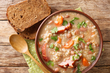Thick rich barley and bean soup with smoked meat and vegetables close-up in a bowl on the table....