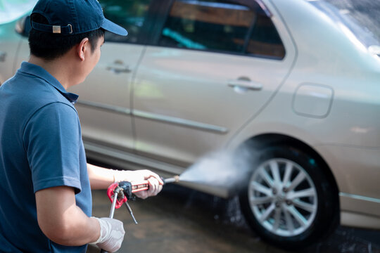 Close Up Of A Man In Uniform Washes His Car With A Large Head Of Water From A Karcher And Washing Car With Soap. Cleaning And Disinfection. Car Wash Service Concept.