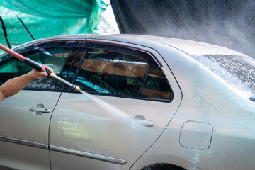 Fototapeta premium Close up photo of a man hands washes his car with a large head of water from a karcher on open air. Cleaning and disinfection. Car wash service concept.