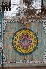 Old Traditional Russian Rustic Gate Fence with Wooden Carvings Ornaments and Weathered Paint against Bare Birch Tree