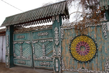 Old Traditional Russian Rustic Gate Fence with Wooden Carvings Ornaments and Weathered Paint against Bare Birch Tree
